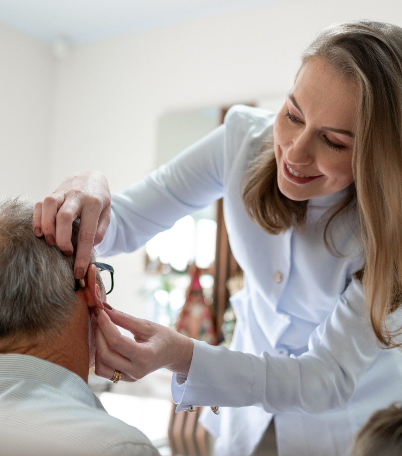 Profissional do Instituto do Ouvido ajustando um aparelho auditivo em um paciente idoso, demonstrando o cuidado e a atenção no processo de adaptação.